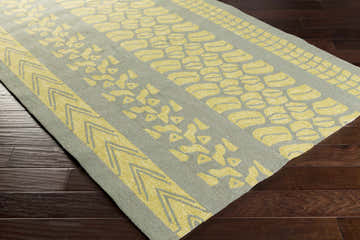 Close up of lime green Houma Area Rug with sage and yellow tribal pattern on dark wood floor. Corner