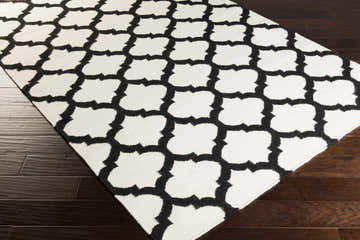 Close-up of the Humeston Area Rug, a hand-woven wool rug with a black and ivory quatrefoil pattern on dark wood floors. Corner