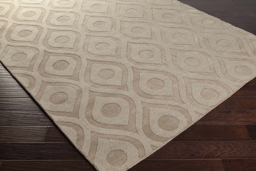 Close-up of the Hundred Area Rug. Tan wool rug with a contemporary, geometric teardrop and circle pattern. Corner