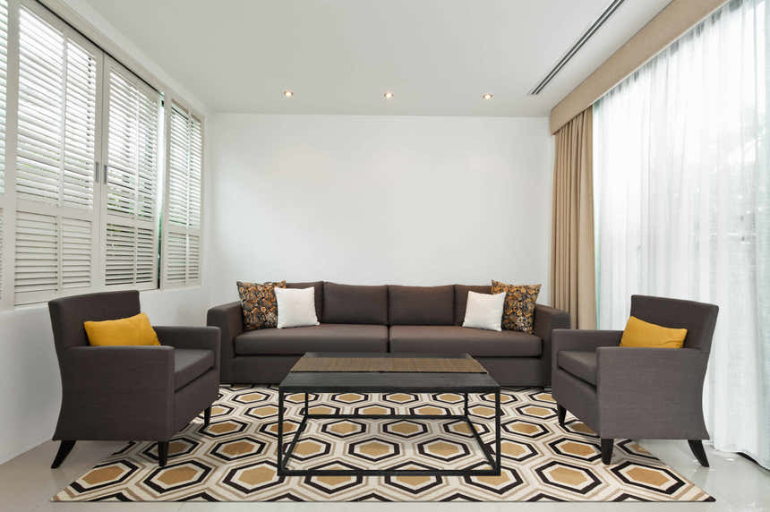 Living room scene with brown sofa and chairs on a Hydeville Area Rug with black, camel, and beige geometric pattern. Roomscene-Rectangle