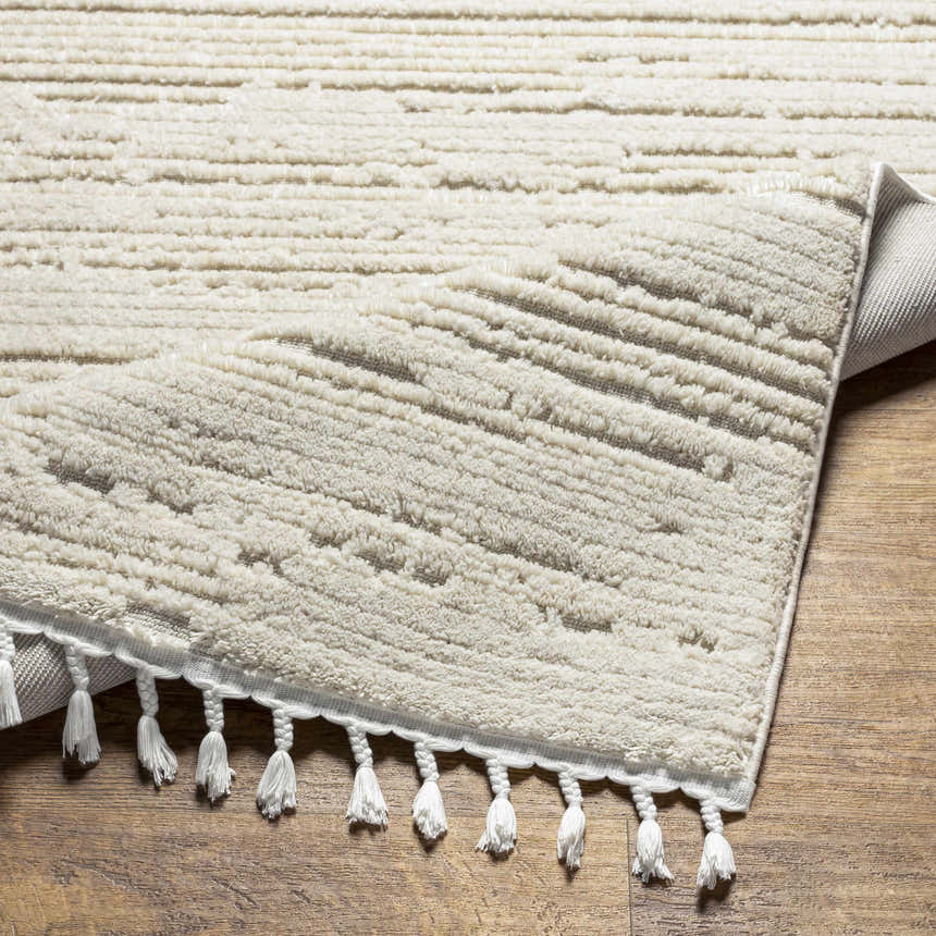Close-up of the Ibarra Textured Ivory Rug, showing its high/low pile, horizontal stripes, and tassel fringe detail. Fold