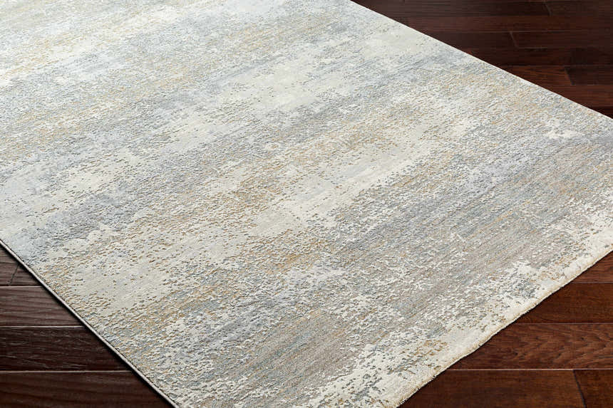 Close-up of the Ikram Thick Luxe Boutique Rug. Abstract design in cloud gray, dark gray, and light gray on dark wood floors. Corner