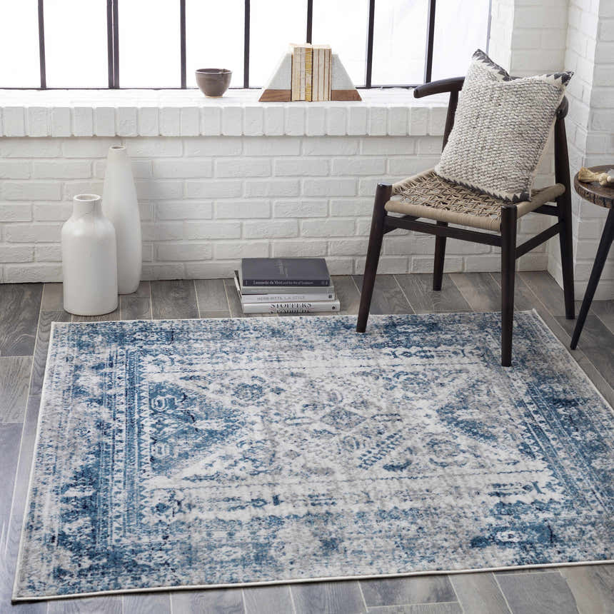 Light-filled room scene with blue and gray Inkom Area Rug, chair, and white brick wall. Roomscene-Square
