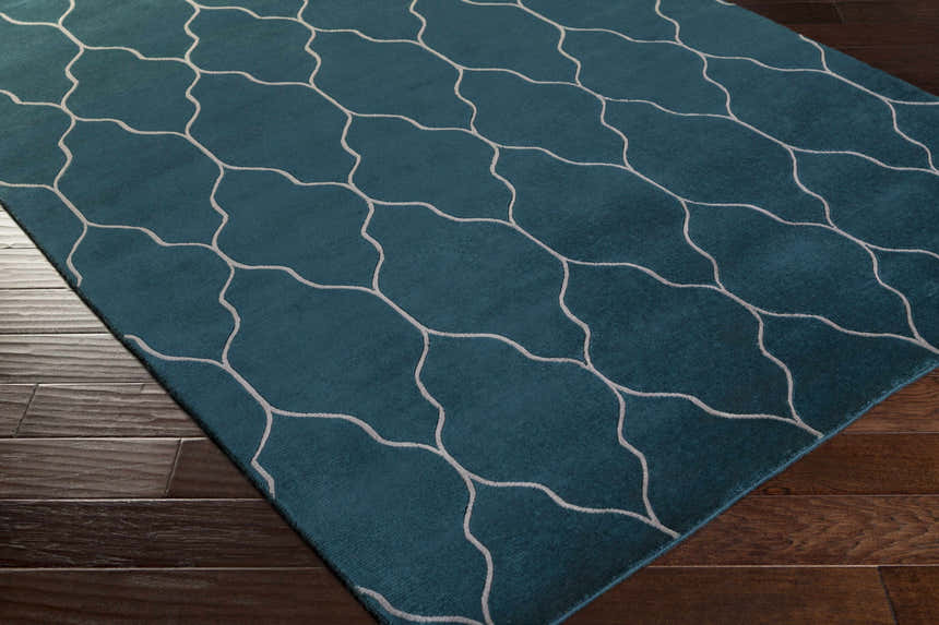 Close-up of the teal Kamay Area Rug with a beige geometric trellis pattern on dark wood floors. Corner