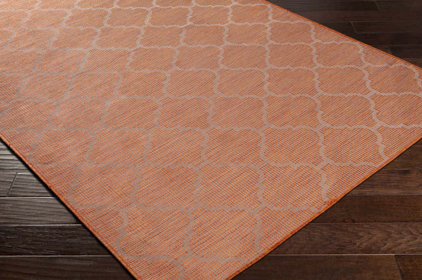 Close-up of Unique Outdoor Trellis Area Rug, rust red color, with a geometric trellis pattern on dark wood floors. Corner