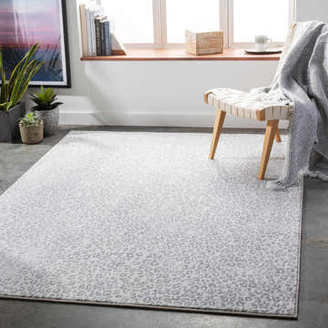 Bright room scene with Keenes Leopard Print Area Rug in charcoal, cream, and light gray. Modern chair and plants. Roomscene-Rectangle