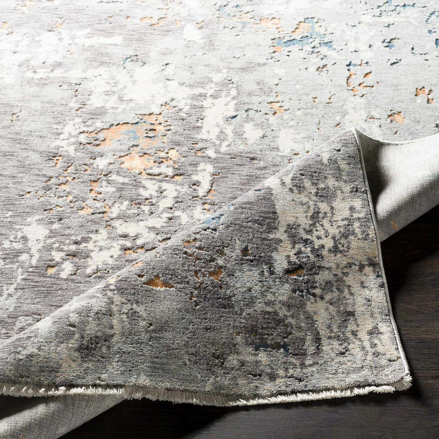 Close-up of the Kenedy Carved Statement Carpet, showcasing its gray, ivory, blue, and orange contemporary design and textured weave. Fold