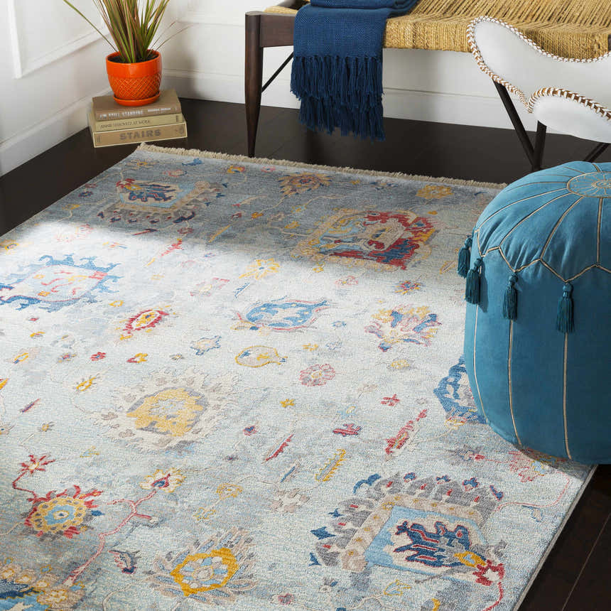 Bohemian room scene with Kernersville Area Rug in blue, orange, and gray. Features a bench, chair, and blue pouf. Roomscene-Rectangle