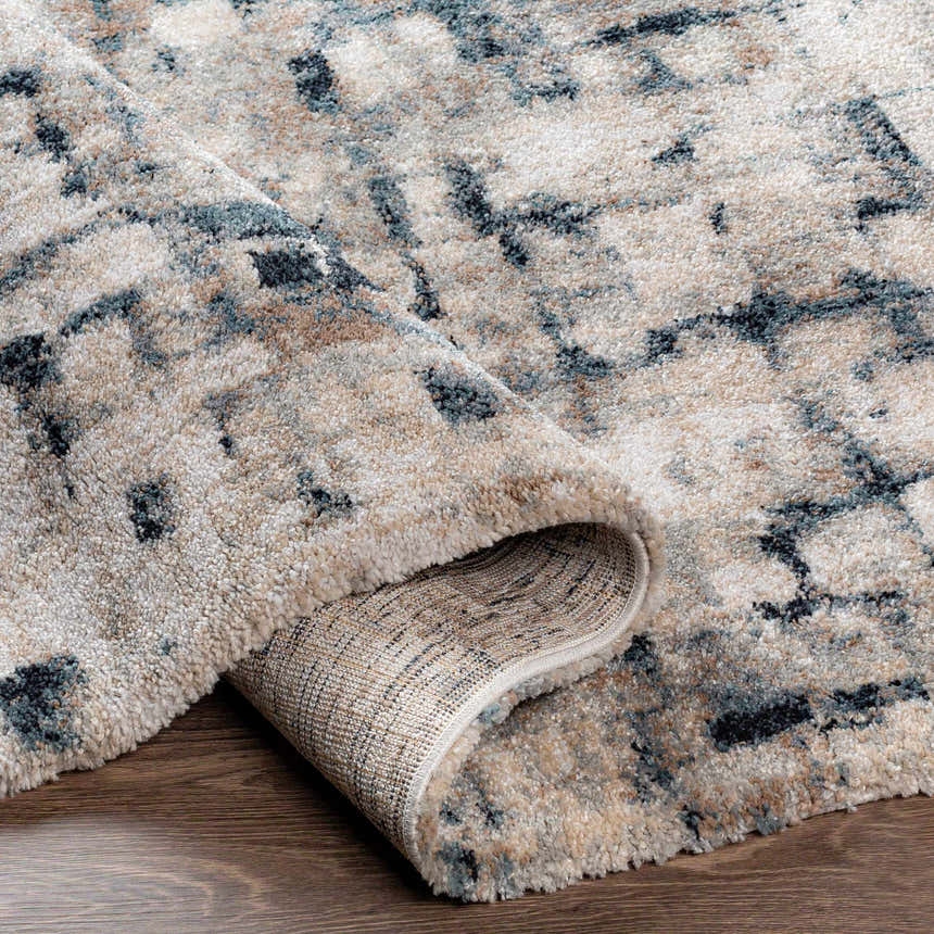 Close-up of the Kilbirnie Area Rug showing its cream, teal, black, and beige contemporary pattern and soft, textured pile. Fold