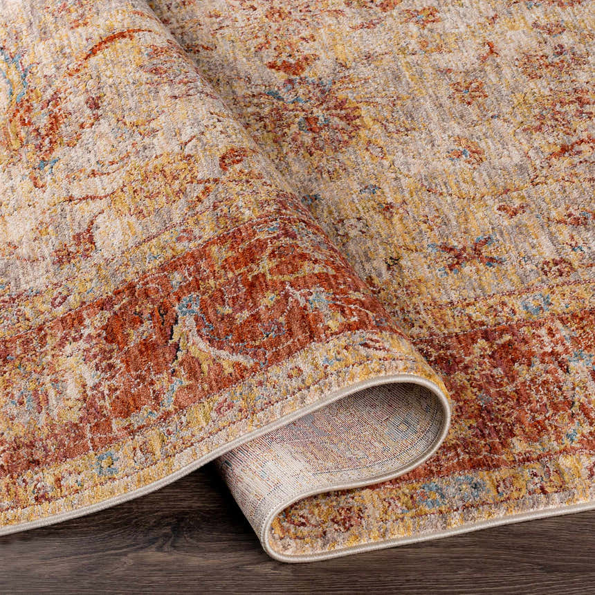 Close-up of the Kilsby Area Rug showing its traditional pattern, warm rust, gold, and beige tones, and soft texture. Fold