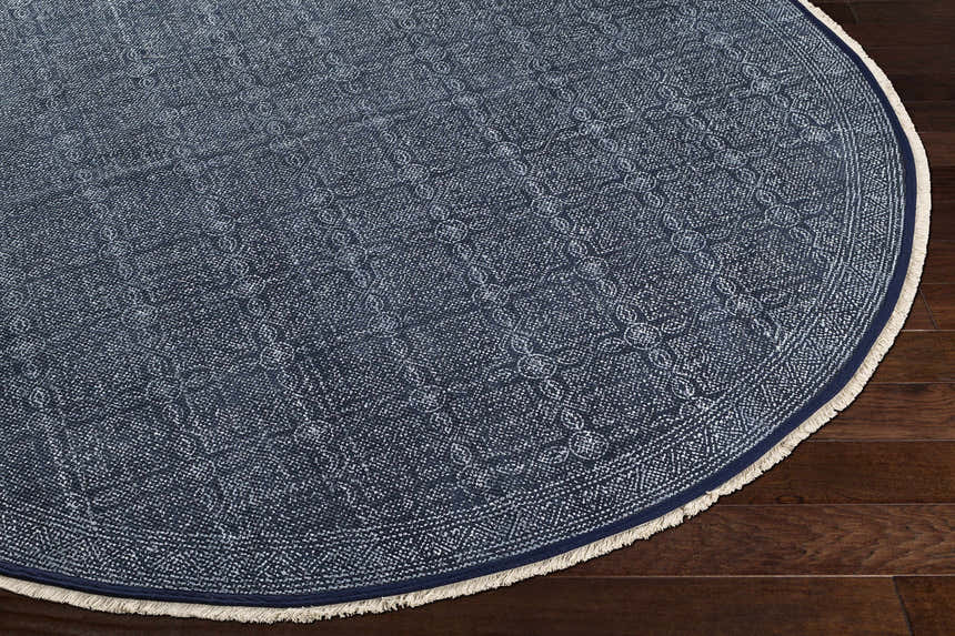 Close-up of the Kilburn Blue Cotton Round Carpet showing its woven texture and bohemian pattern on dark wood floors. Corner