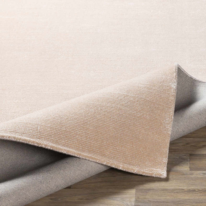 Close-up of the peach Klickitat Area Rug showing the hand-loomed texture and backing on a wood floor. Fold