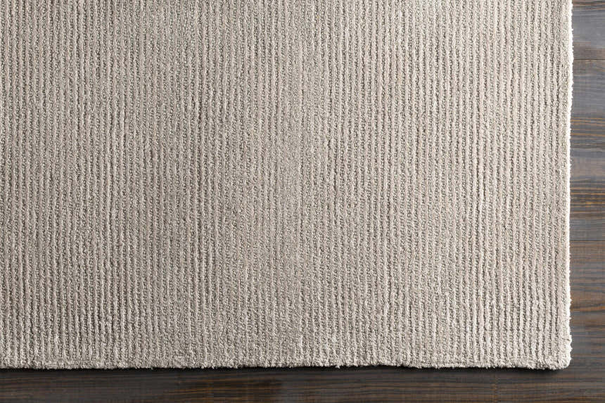 Close-up of the light gray Keller Area Rug showing its striped design and hand-tufted texture on dark wood floor. Corner
