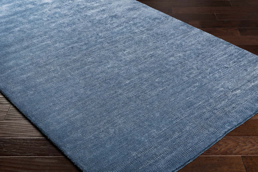 Close-up of the blue Kendall Carpet showing its hand-knotted texture and subtle pattern on dark wood flooring. Corner
