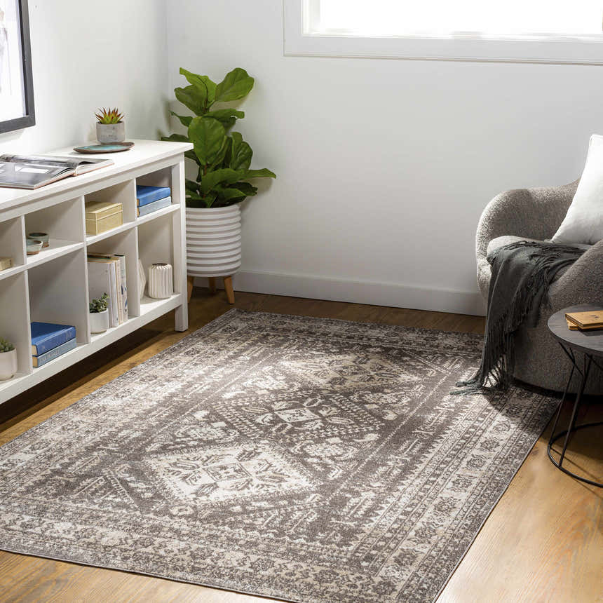 Living room scene with a cream and brown Kingscourt Washable Area Rug, white shelving, gray chair, and wood floors. Roomscene-Rectangle