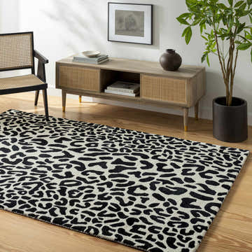 Living room scene with a black and off-white Kass Leopard Print Area Rug, wood floors, console table, and chair. Roomscene-Rectangle