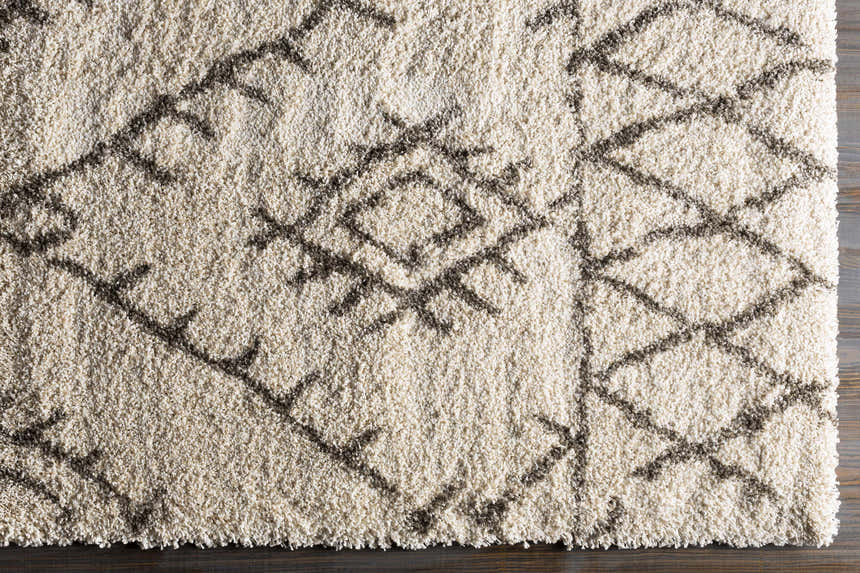 Close-up of the Kunia Area Rug. Shag rug with a charcoal geometric pattern on an ivory and light beige background. Corner