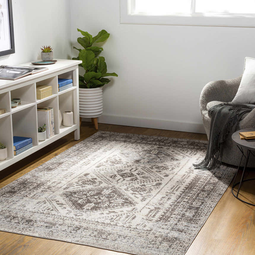 Living room scene with a brown and beige Ladybrand Washable Area Rug, white shelving unit, gray chair, and wood floors. Roomscene-Rectangle