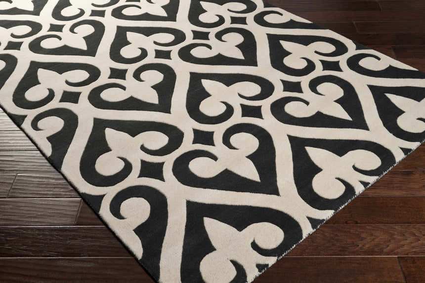 Close-up of the Landa Area Rug. Black and cream, hand-tufted wool rug with a modern, geometric pattern on dark wood flooring. Corner