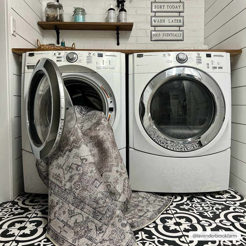 Farmhouse laundry room with Athor Washable Rug being put in the washing machine. Black and white patterned tile floor. Washing-Machine
