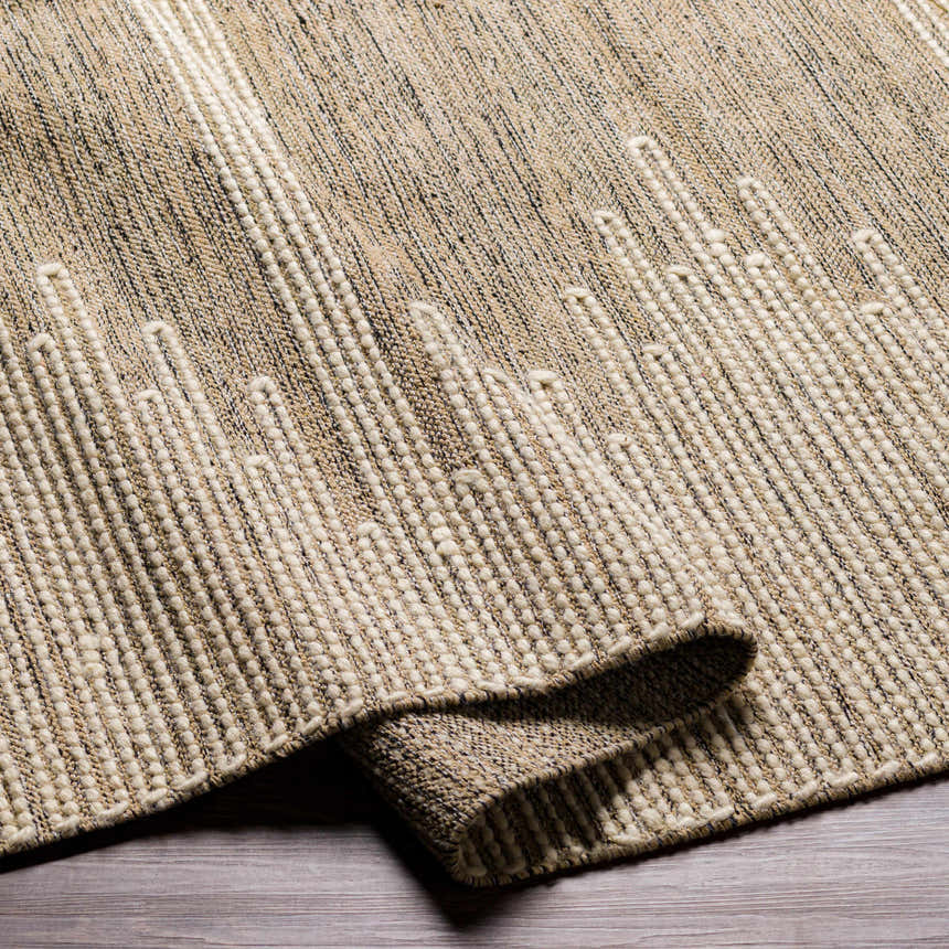 Close-up of the hand woven Lucasville Area Rug, showing its beige, cream, and black fibers and textured, geometric pattern. Fold