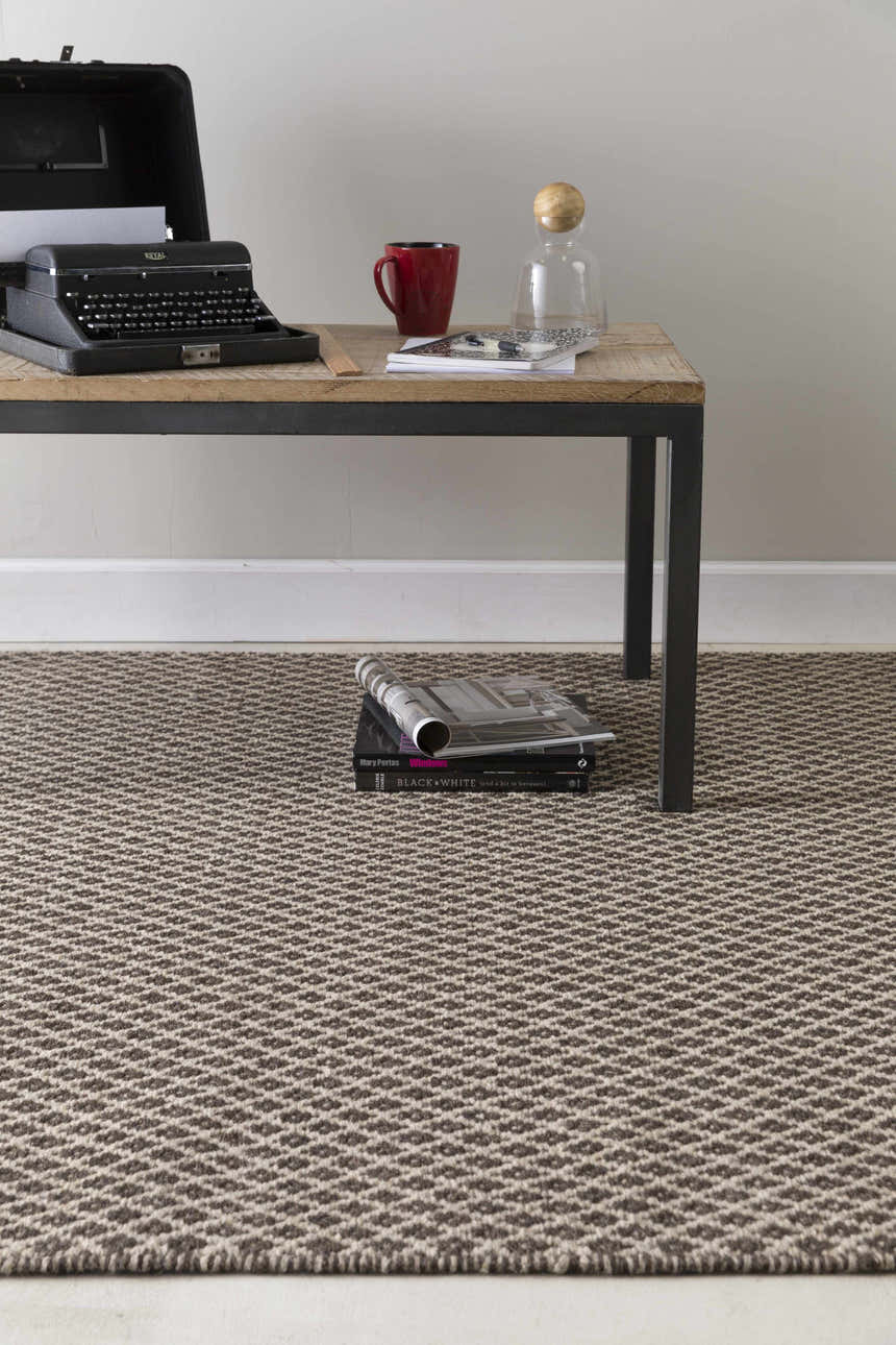Living room scene with a Lingo Brown Trellis rug under a table with a typewriter, books, and coffee mug. Styleshot