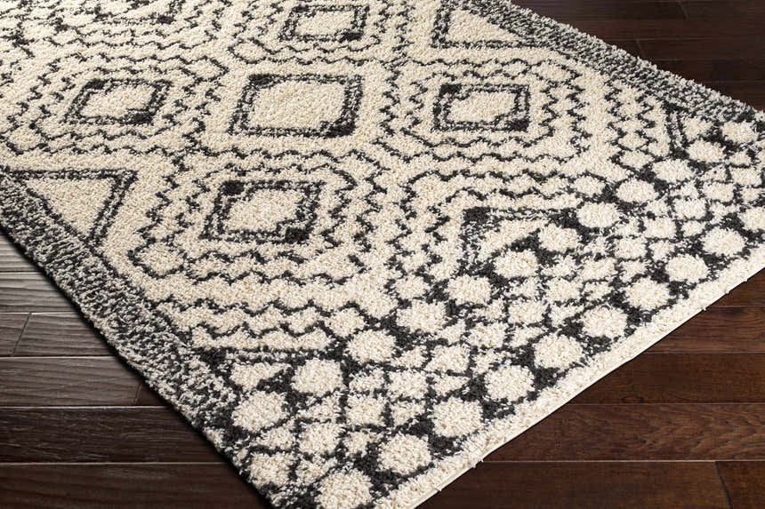 Close-up of the Lloydminster Area Rug. Black and cream shag rug with a geometric Moroccan-inspired pattern. Corner
