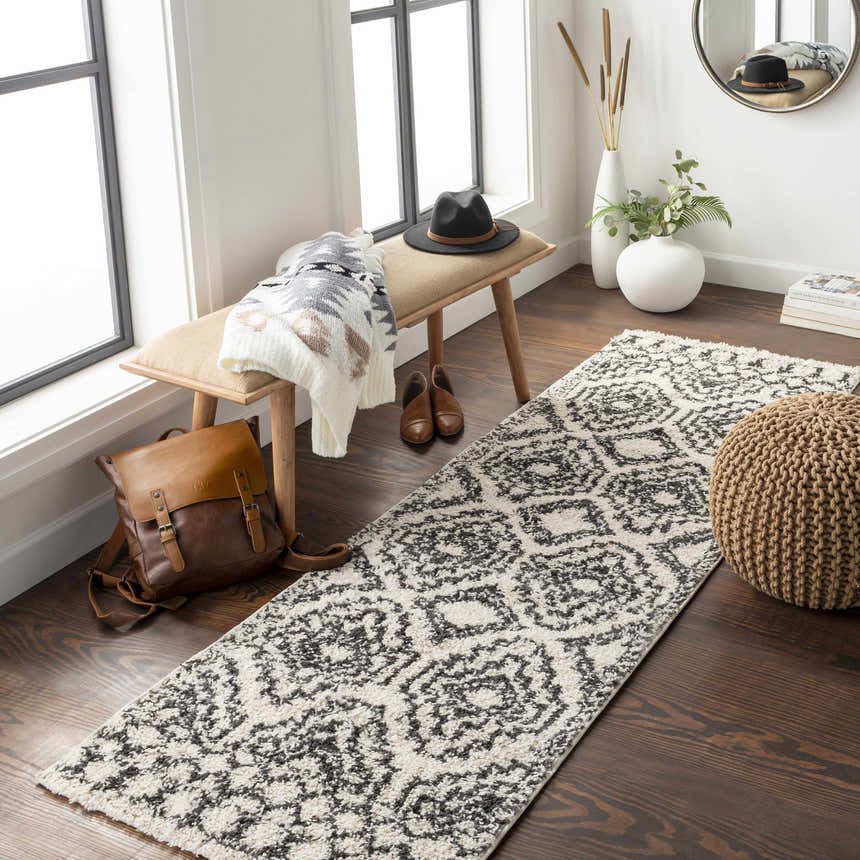 Entryway scene with a black and cream Lloydminster Area Rug runner, bench, and brown leather backpack. Roomscene-Runner
