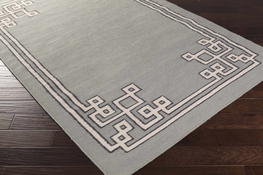 Close-up of the Lott Area Rug. Gray wool rug with ink blue and light gray geometric border pattern. Corner