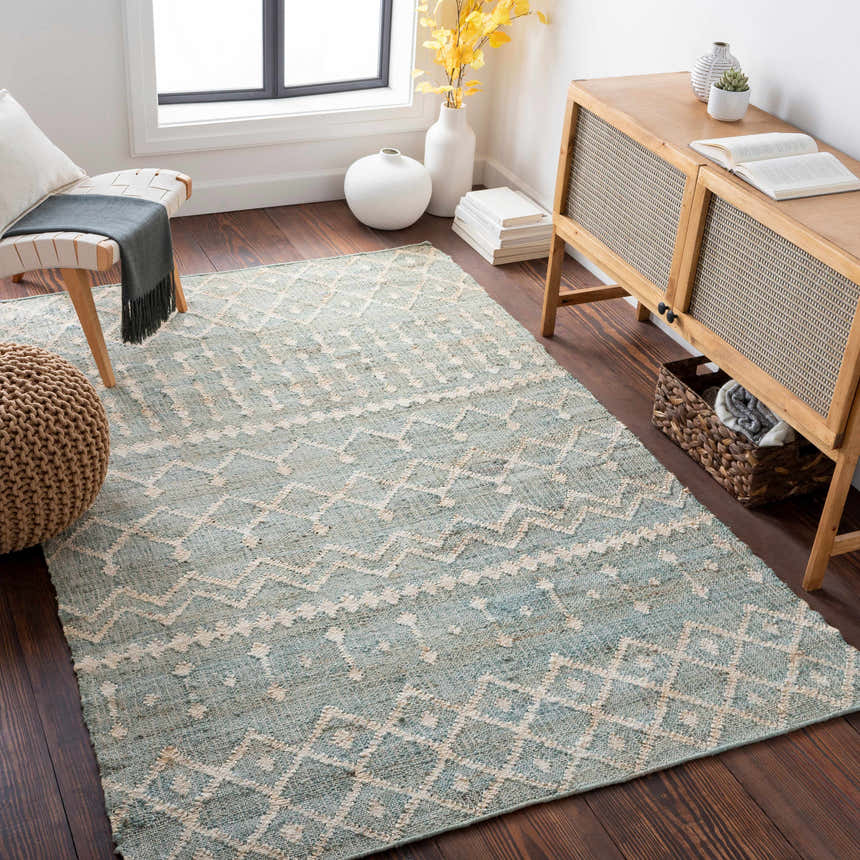 Living room scene with a dusty sage Lowville Jute Rug, wooden cabinet, woven pouf, and dark wood floors. Roomscene-Rectangle