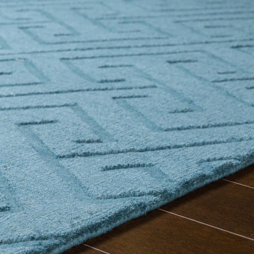 Close-up of the teal Ludden Area Rug showing its geometric pattern and hand-loomed wool texture on a wood floor. Texture
