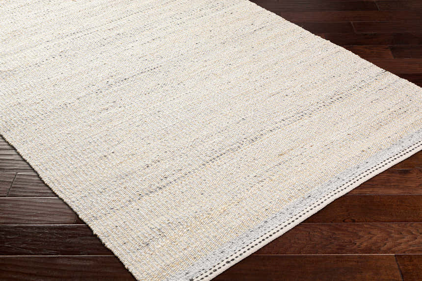 Close-up of the hand woven Lumatil Area Rug. Jute and wool rug in cream, light beige, and light gray on dark wood floors. Corner