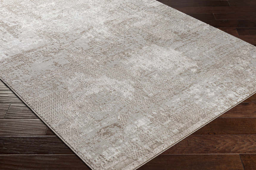 Close-up of the Lumbia Distressed Embossed Area Rug. Neutral beige tones with a subtle, textured pattern on dark wood flooring. Corner