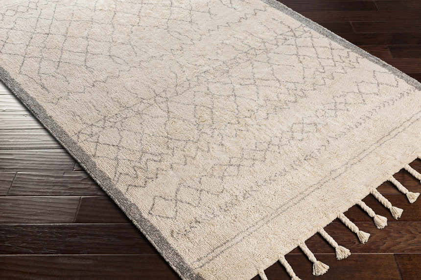 Close-up of the cream and gray Luncarty Area Rug with geometric pattern and tassels on dark wood floors. Corner