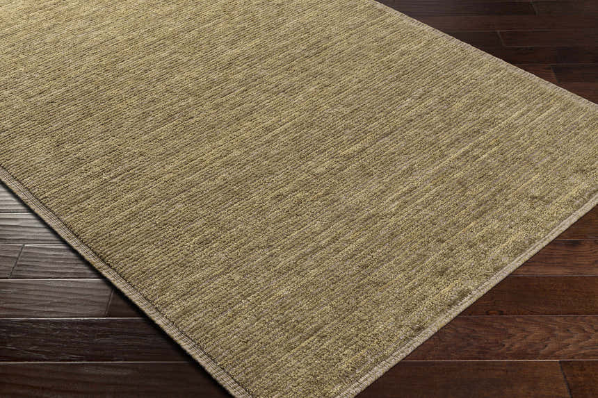 Close-up of the hand-loomed Magpet Area Rug in olive. 100% wool rug with subtle texture on dark wood floors. Corner
