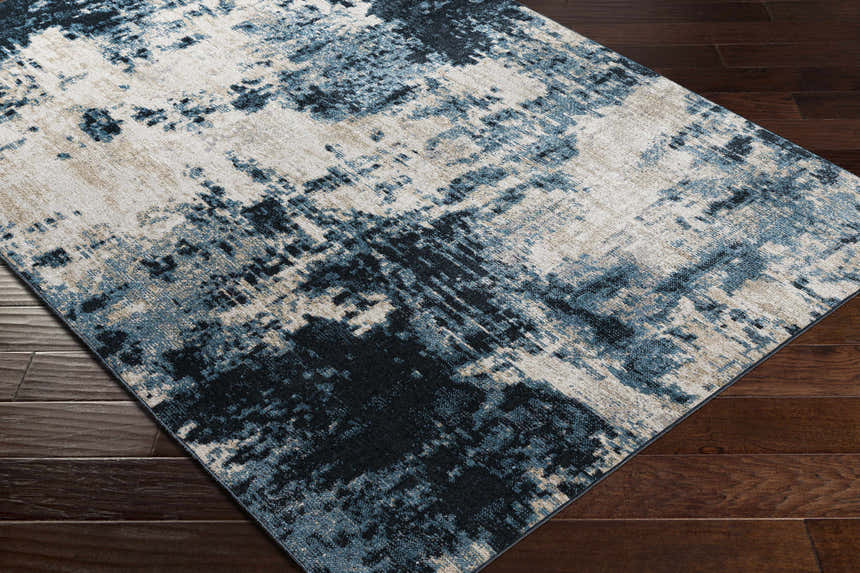 Close up of the Masiga Washable Area Rug. Contemporary style with blue, black, and beige abstract pattern on a dark wood floor. Corner