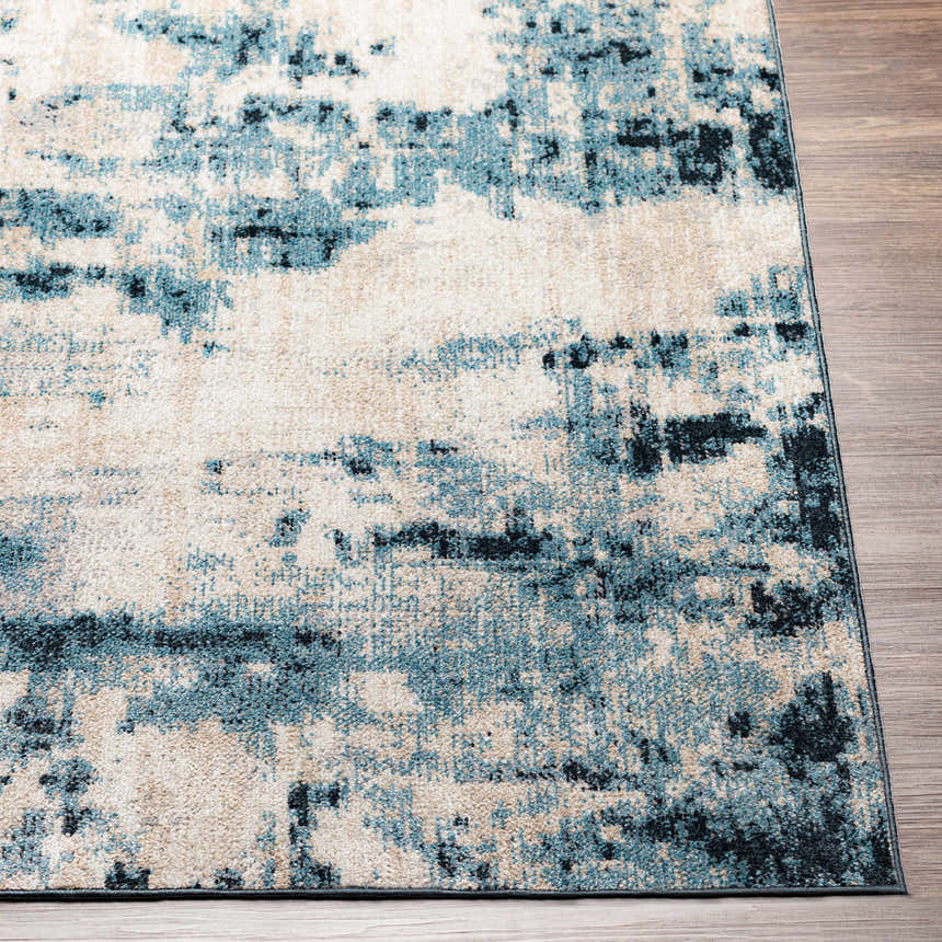 Close up of Masiga Washable Area Rug showing abstract design in shades of blue, beige, and black on wood floor. Front