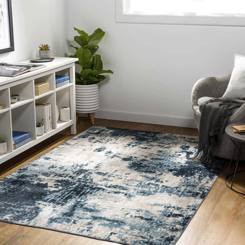 Living room scene with a blue and beige Masiga Washable Area Rug, white shelving unit, gray chair, and wood floors. Roomscene-Rectangle