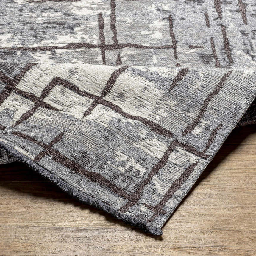 Close-up of the Mace Area Rug, showcasing its charcoal, cream, and slate colors and geometric pattern. Fold