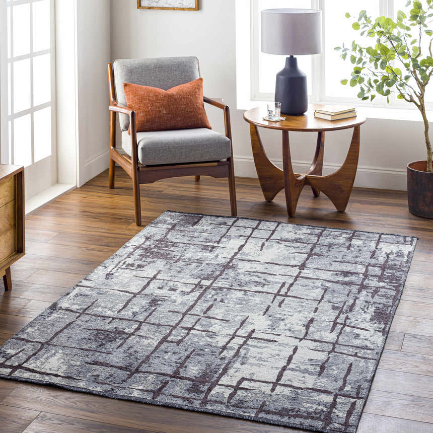 Living room scene with a charcoal and cream Mace Area Rug, gray chair, and mid-century modern decor. Roomscene-Rectangle