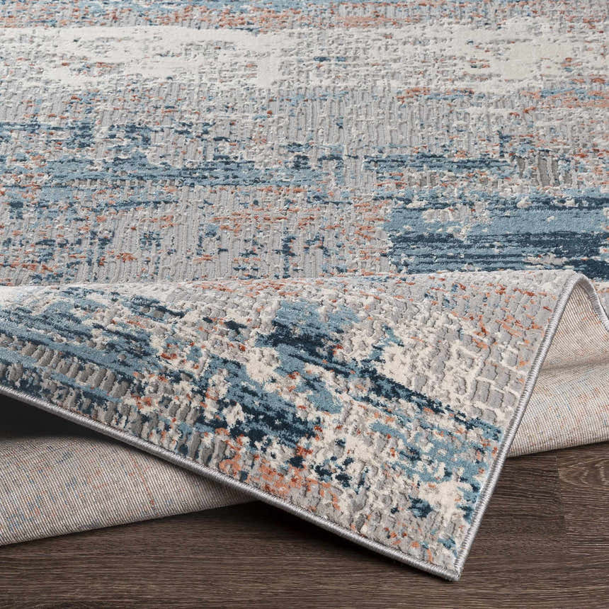 Close-up of McCracken Area Rug showing abstract blue, gray, and peach pattern and textured weave. Fold