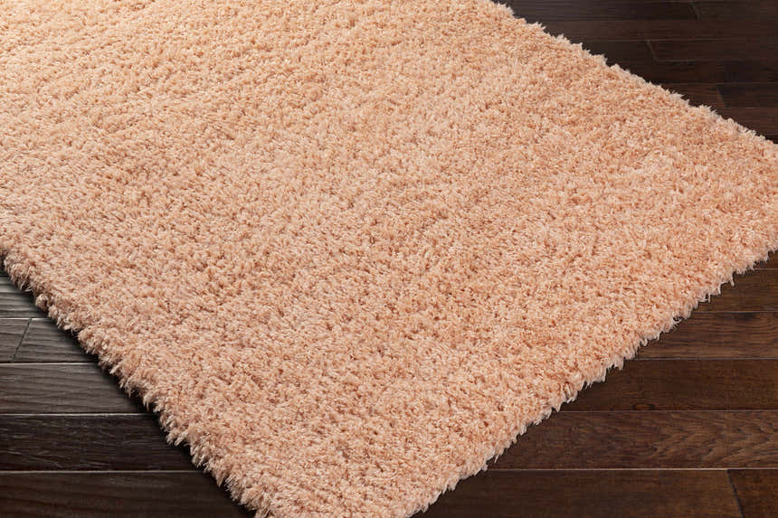 Close-up of the Siari Peach Shag Rug showing its plush texture and soft peach color on a dark wood floor. Corner