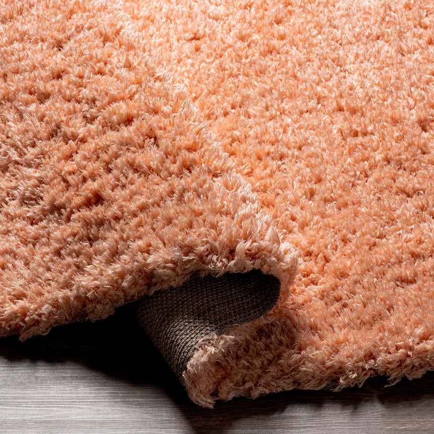 Close-up of the plush texture and color of the Siari Peach Shag Rug. The rug's backing is visible. Fold