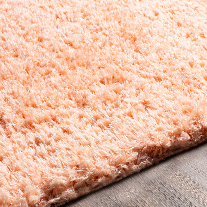Close-up of the Siari Peach Shag Rug showing its soft, fluffy texture and warm peach color on a wood floor. Texture
