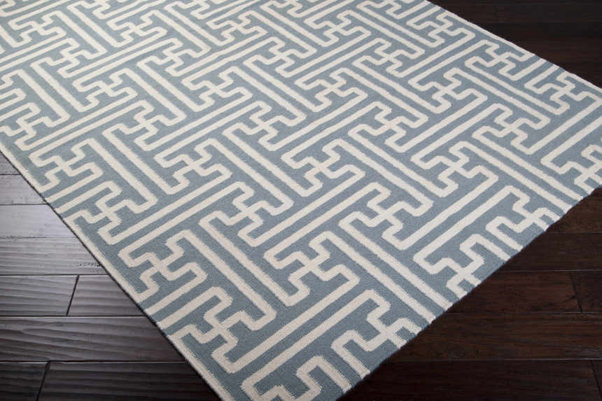Close-up of the Metuchen Area Rug. Light beige and light blue geometric pattern on a hand woven wool rug. Corner