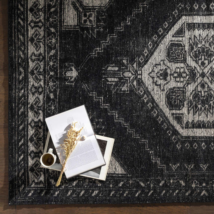 Close-up of the black and cream Minapan Premium Area Rug with a traditional oriental pattern and a cup of coffee on top. Styleshot