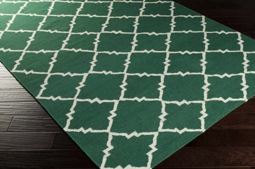 Close-up of the Minehead Area Rug. Dark green wool rug with a light gray geometric trellis pattern on dark wood floors. Corner