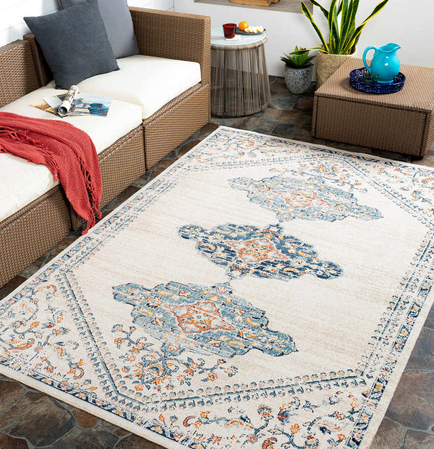 Cozy patio scene with a Mistissini Area Rug in aqua, cream, and blue, styled with wicker furniture and a coral throw blanket. Roomscene-Rectangle