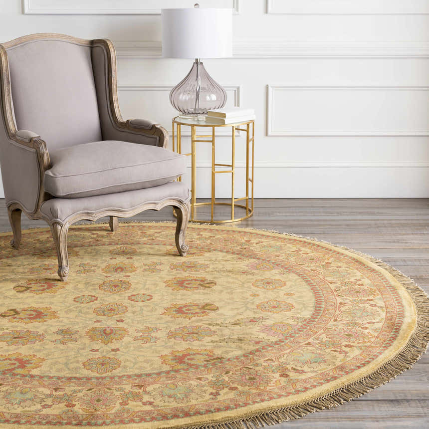 Living room scene with a round Maurice Area Rug in brick red, brown, and mustard under a gray chair and gold side table. Roomscene-Round
