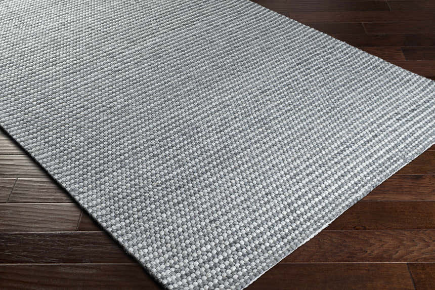 Close-up of the hand woven Mulgoa Area Rug in medium gray, showing its textured, contemporary design on dark wood floors. Corner
